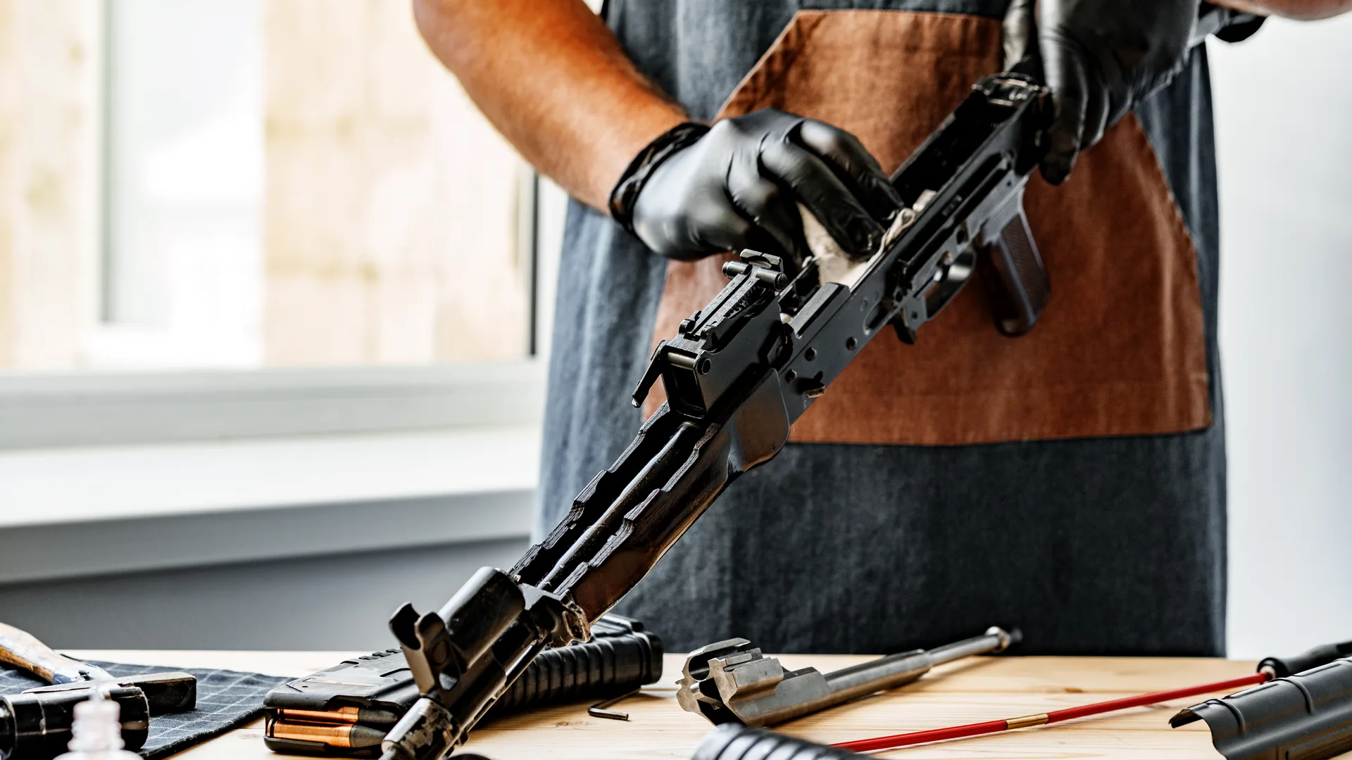 Hände zerlegen ein Gewehr an der Werkbank, Werkstattkurs Waffentechnik